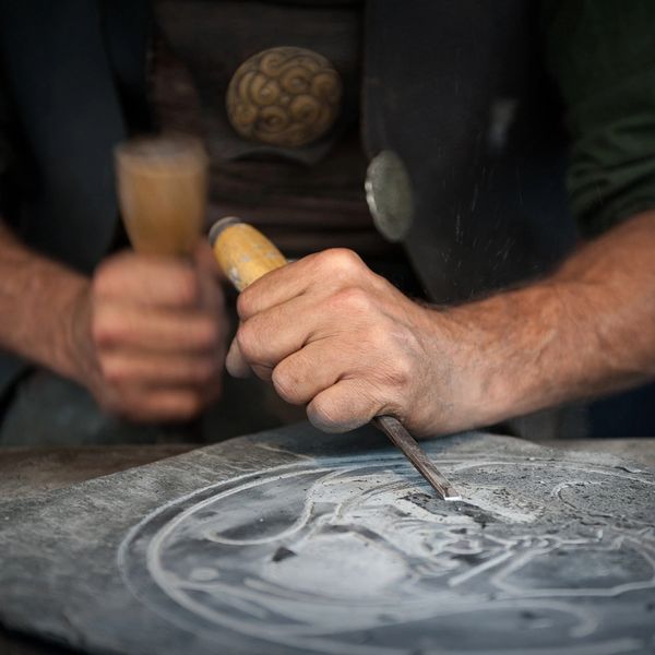 Close-up of a craftsman carving a stone surface with a chisel and hammer.