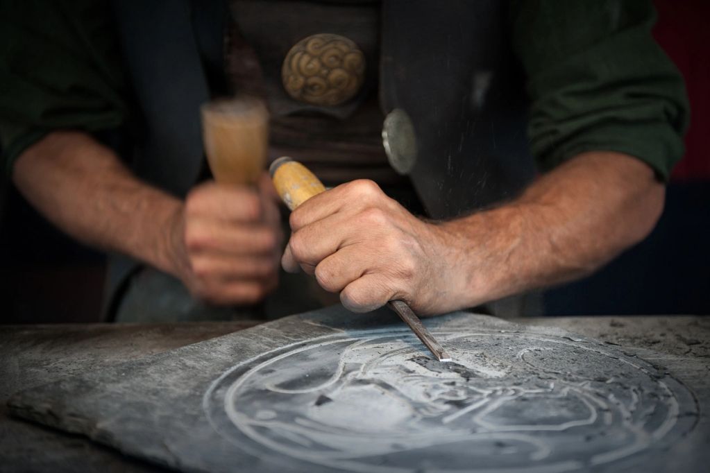 Craftsman carving detailed design into stone with chisel and hammer.