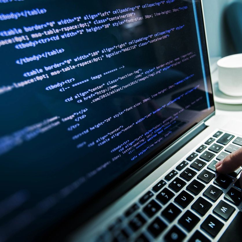 Close-up of a laptop screen displaying HTML code with a hand typing on the keyboard.