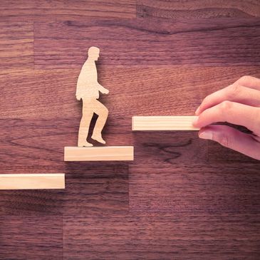 Wooden figure climbing steps held by a hand.