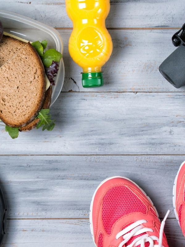 Lunch sandwich, orange juice, and pink sneakers on a wooden surface.