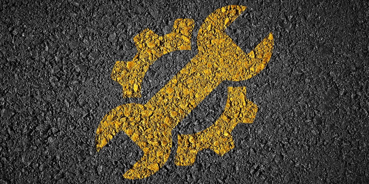 Yellow wrench and gear symbol painted on asphalt.