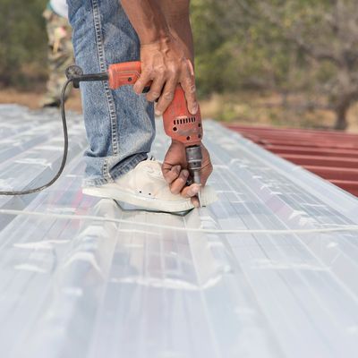 roofer installing metal screwa into a metal roof with a drill