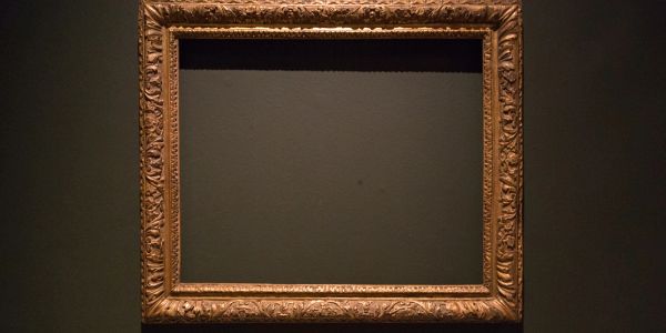 Empty ornate golden picture frame on a dark wall.