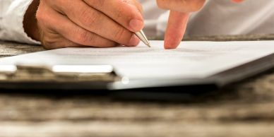 Hand holding pen and pointing at paper on clipboard.