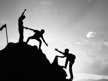 Three people demonstrating teamwork helping each other climb to the top of a hill / mountain.