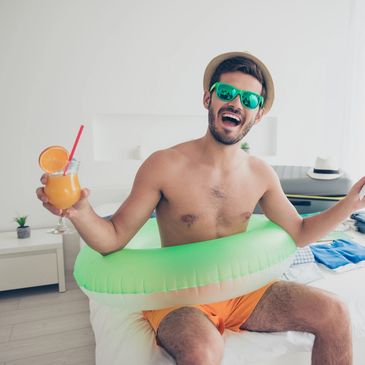 Happy man with hat and fruity drink with a straw sporting beach toys and sunglasses.