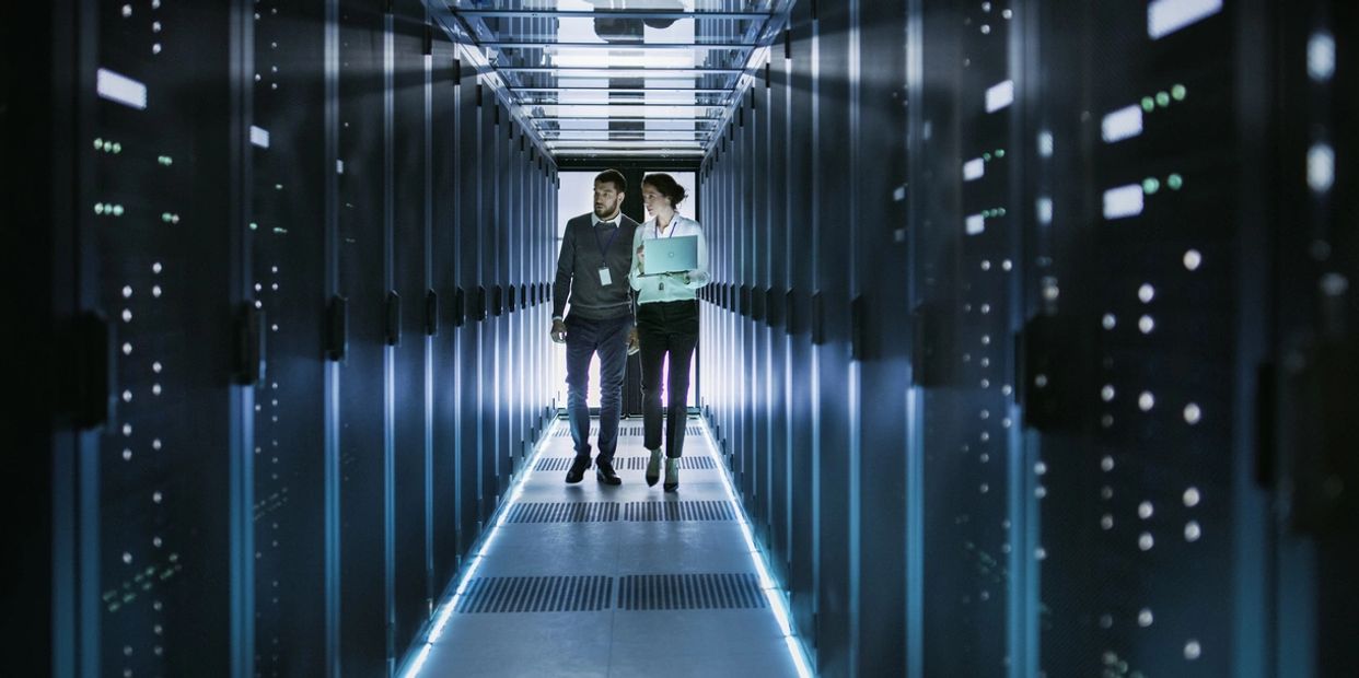 Two IT professionals walk through a glowing server room aisle.