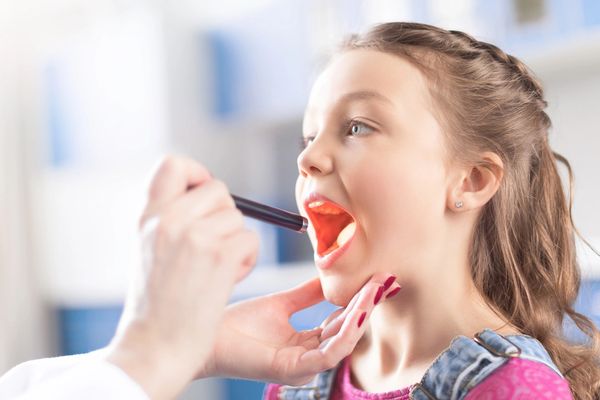 Doctor examining young girl's throat with a flashlight.