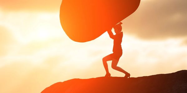 Silhouette of a person carrying a large rock at sunset on a cliff.