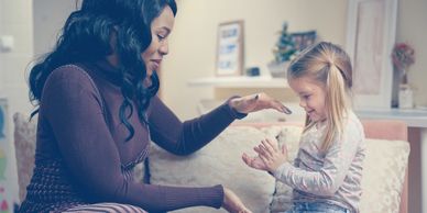 Woman and child playing a hand game while sitting on a couch.