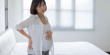 Pregnant woman with hand on belly and experiencing back pain and labor pain.
