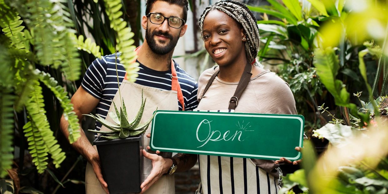 man and woman in florist shop holding plant and open sign