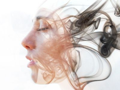 Profile of a woman’s face blending into swirling smoke patterns.