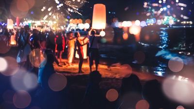 People releasing a glowing sky lantern at night on a beach.