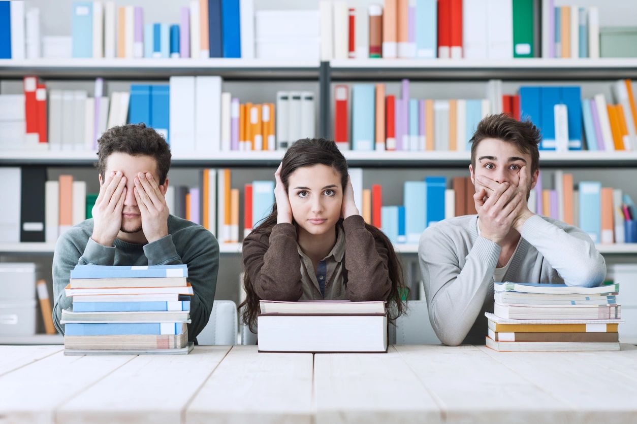 Three people seated with their books, as one covers their eyes, one covers their ears and one covers their mouth.
