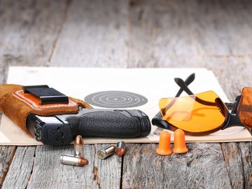 gun in a holster with a paper target and shooting glasses and hearing protection and ammo