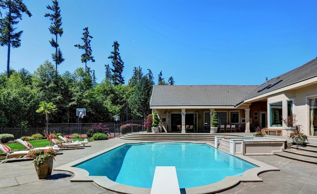 A spacious backyard with a custom swimming pool and lounge chairs under a clear blue sky.