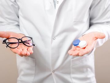 Doctor holding glasses in one hand and contact lens cases in the other.
