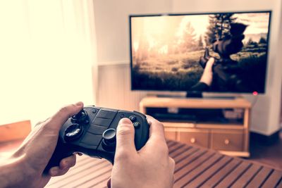 Person playing a video game, controller in-hand. TV is next to a bright window or door. There is a l