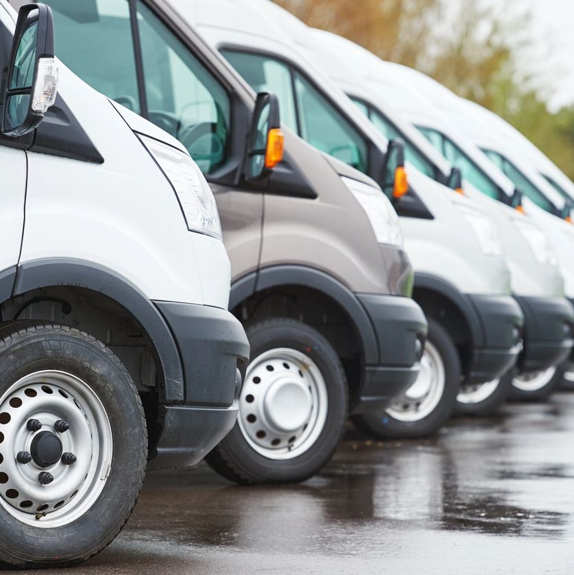 A row of white vans parked on a wet surface outdoors.