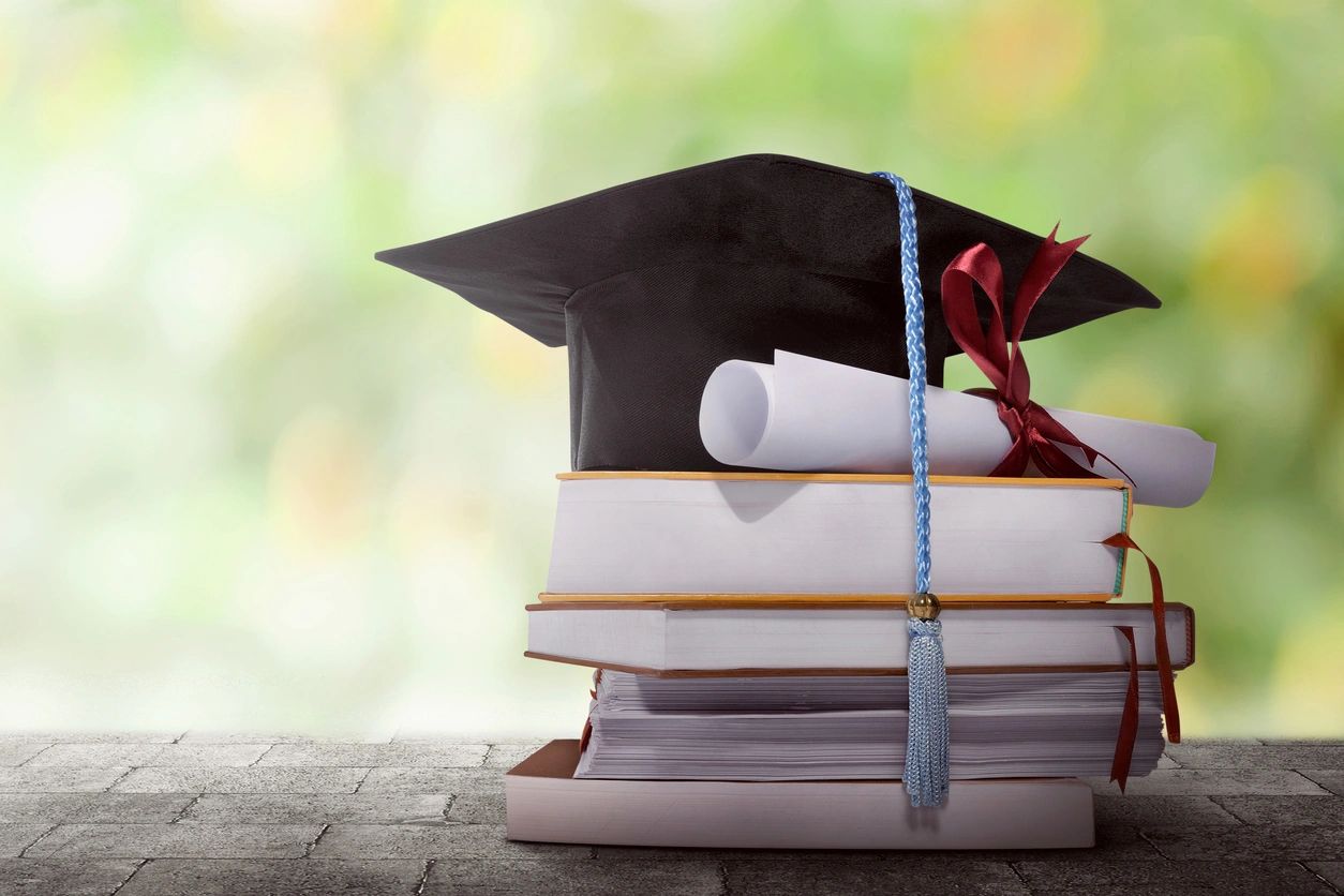 Graduation hat, and diploma atop a stack of books.