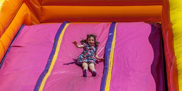 Young girl sliding down a colorful inflatable slide outdoors.