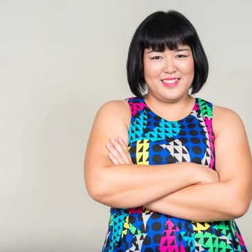 An East Asian woman with her arms crossed while smiling and a bob haircut