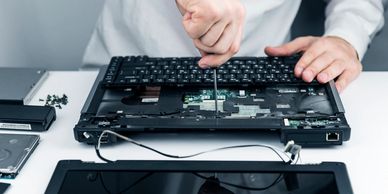 Person repairing a laptop by unscrewing its components on a white table.