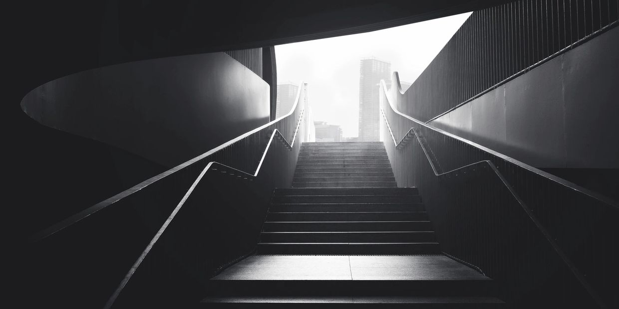 Monochrome photo of stairs leading to a bright cityscape with modern buildings.