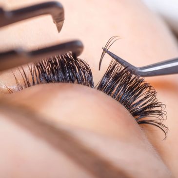 Close-up of eyelash extensions being applied with tweezers.