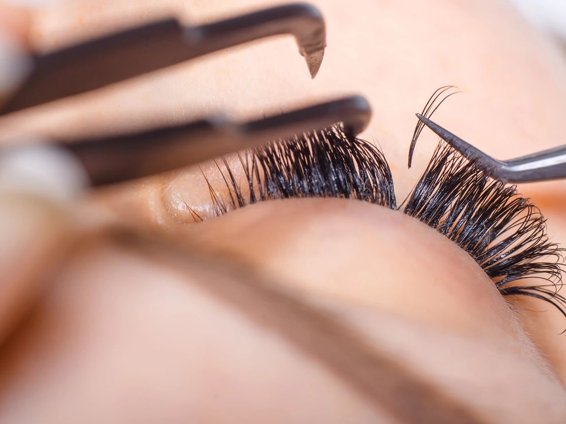 Close-up of eyelash extension application using tweezers.