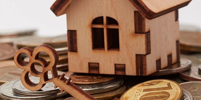 Wooden house model and key on coins symbolizing real estate investment.