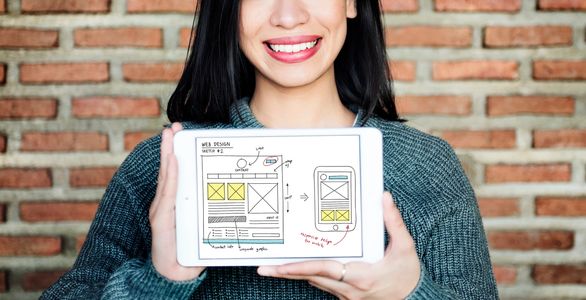 Frau zeigt Webdesign Skizze auf Tablet.
