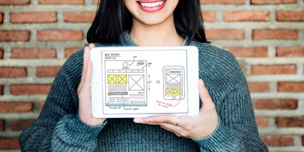 Smiling woman holds tablet with a web design wireframe sketch.