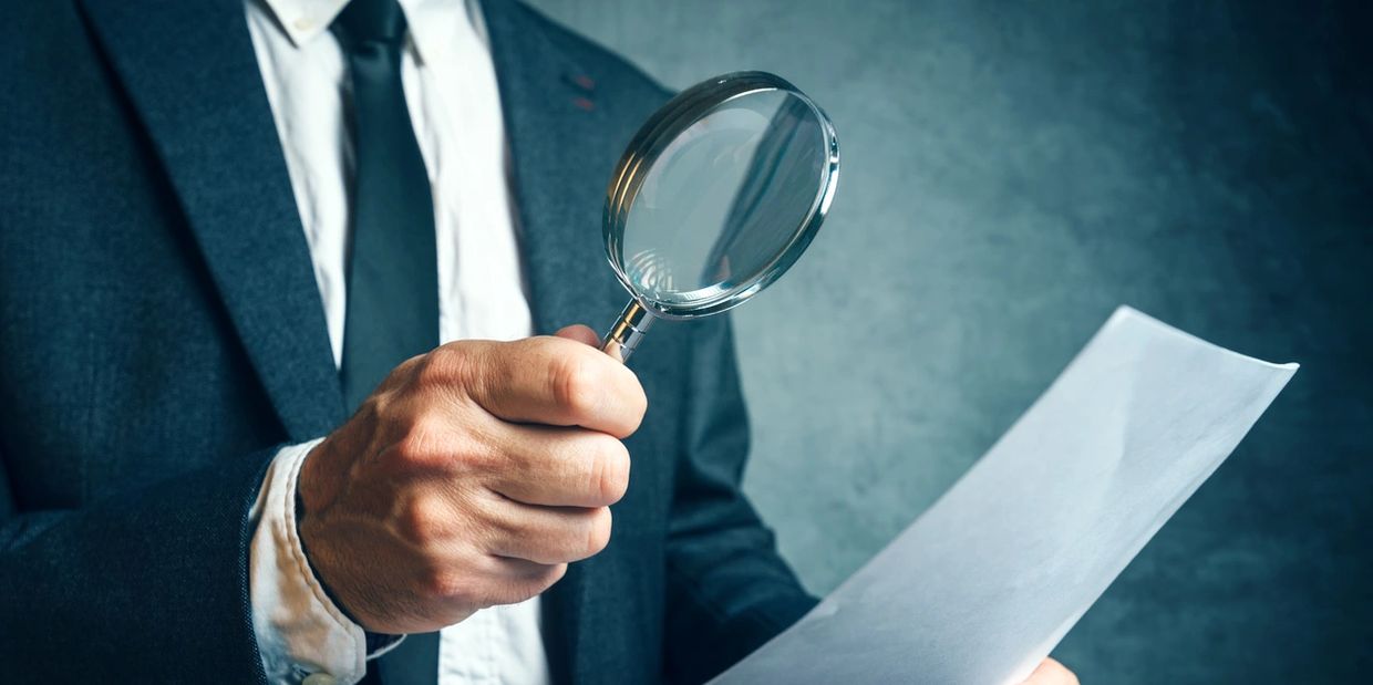 Man in suit examining a document with a magnifying glass.