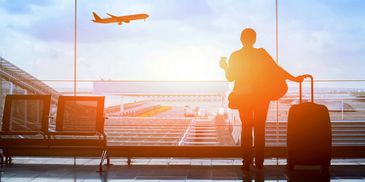 Traveler at airport watching a plane take off during sunrise.