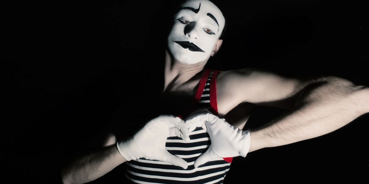 Mime artist in striped outfit making a heart shape with gloved hands.