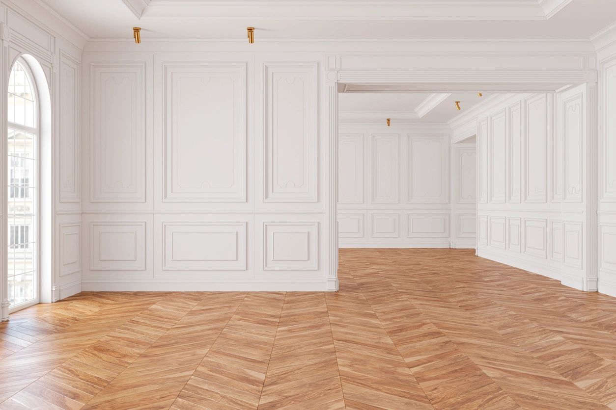 Elegant empty room with white paneled walls and herringbone wood floor.