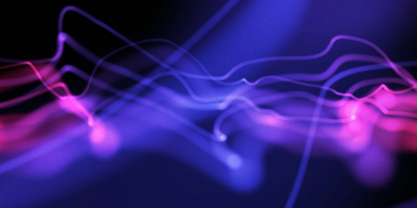 Abstract neon light trails in blue and pink on a dark background.