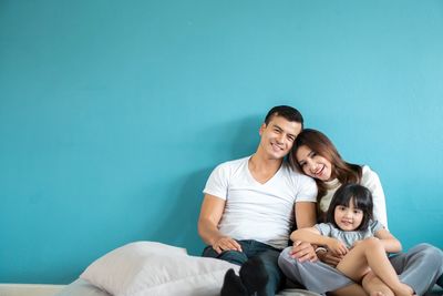 Happy family sitting together against a blue wall.