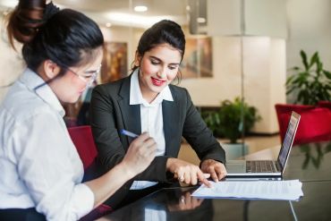 Two women collaborating over documents in an office.