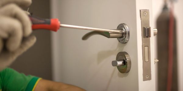 Person using screwdriver to fix a door handle.