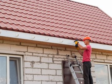 man on ladder installing gutter hooks