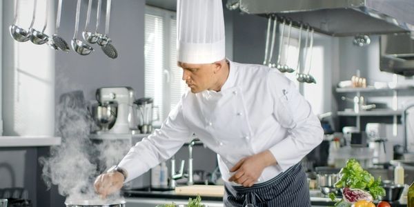 Professional chef in uniform carefully preparing a dish in a restaurant kitchen.