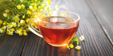 A glass cup of herbal tea on a wooden table with chamomile flowers.