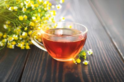 A glass cup of tea with yellow flowers on a wooden table.