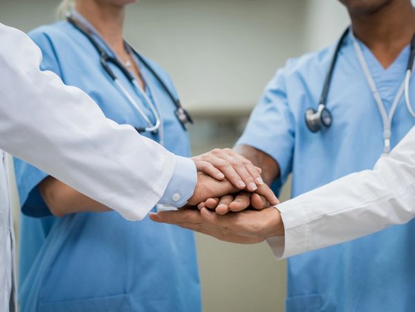 Healthcare professionals stacking hands in teamwork gesture.
