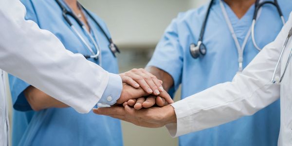 Healthcare professionals with hands stacked on top of each other, symbolizing unity and teamwork.