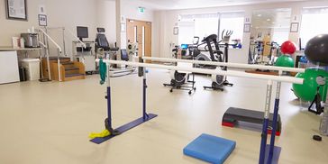 Physical therapy room with exercise equipment and parallel bars.